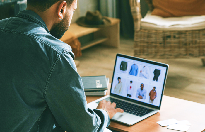 Eine Person, die auf einem Laptop in einem Online-Shop stöbert, wobei verschiedene Hemden auf dem Bildschirm angezeigt werden.